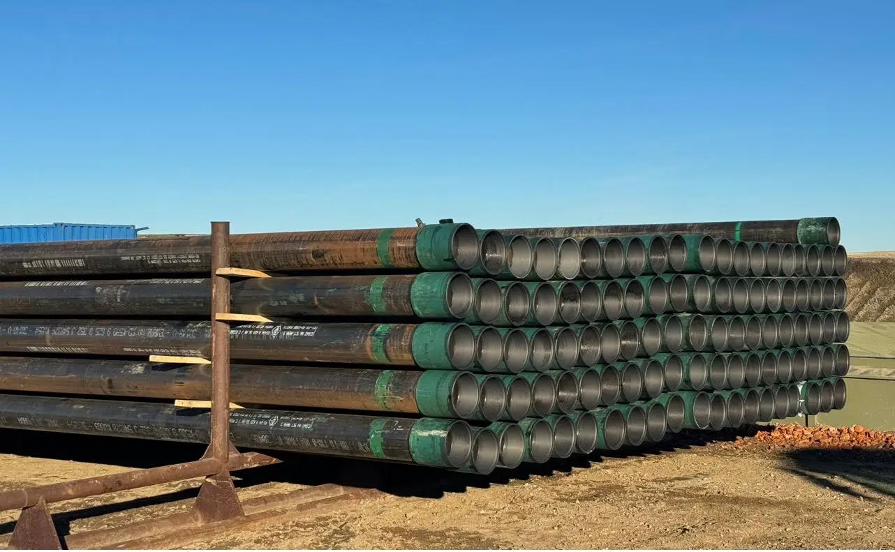 Casing pipe joints with green paint bands stacked on a yard rack under a clear blue sky