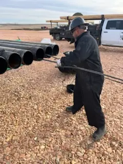 WOS crew member drifting a length of casing on the pad in cold-weather coveralls