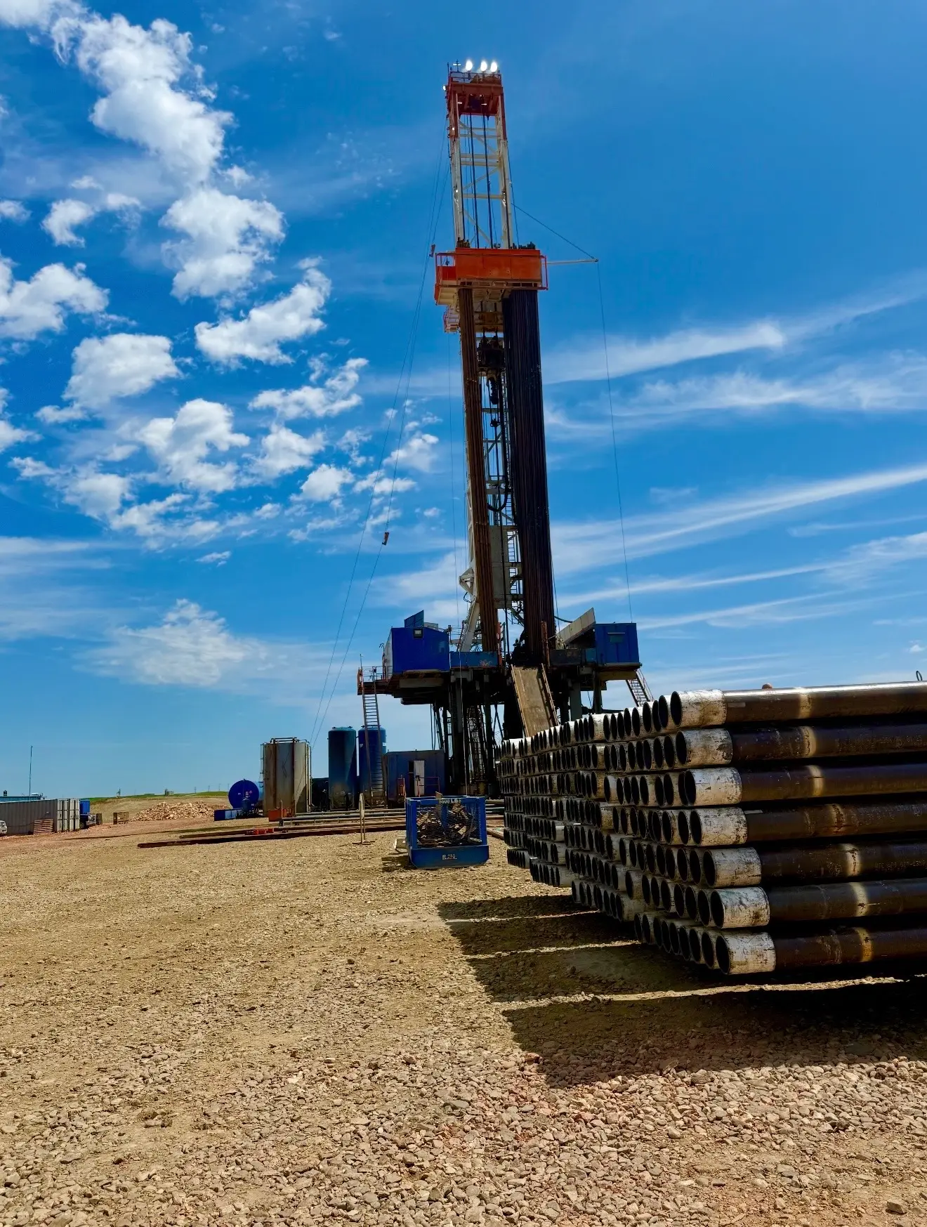 Workover rig and stacked casing tubing on a Bakken pad under a bright blue sky