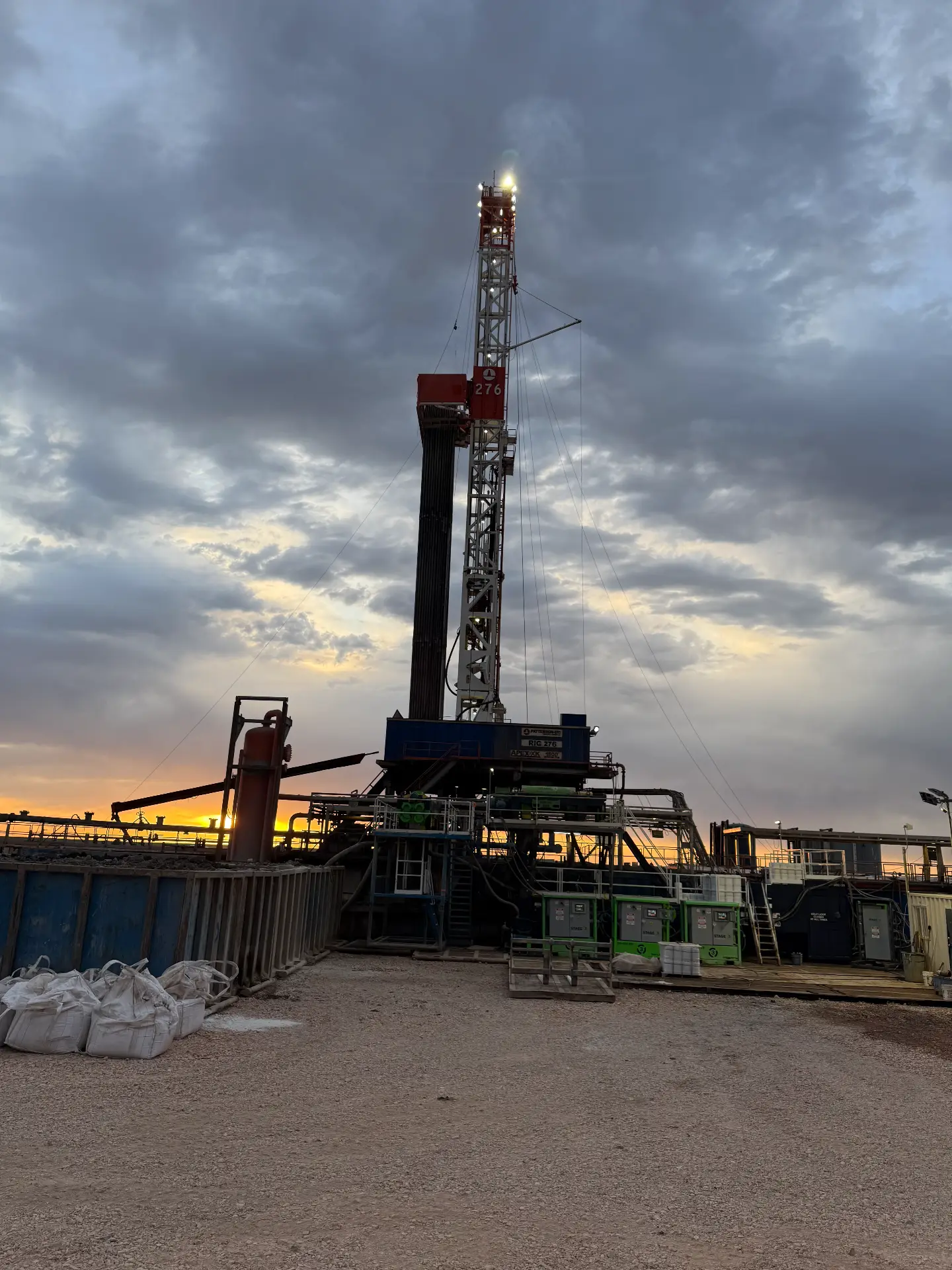 Drilling rig lit at sunset on a Bakken location with WOS-supported crews