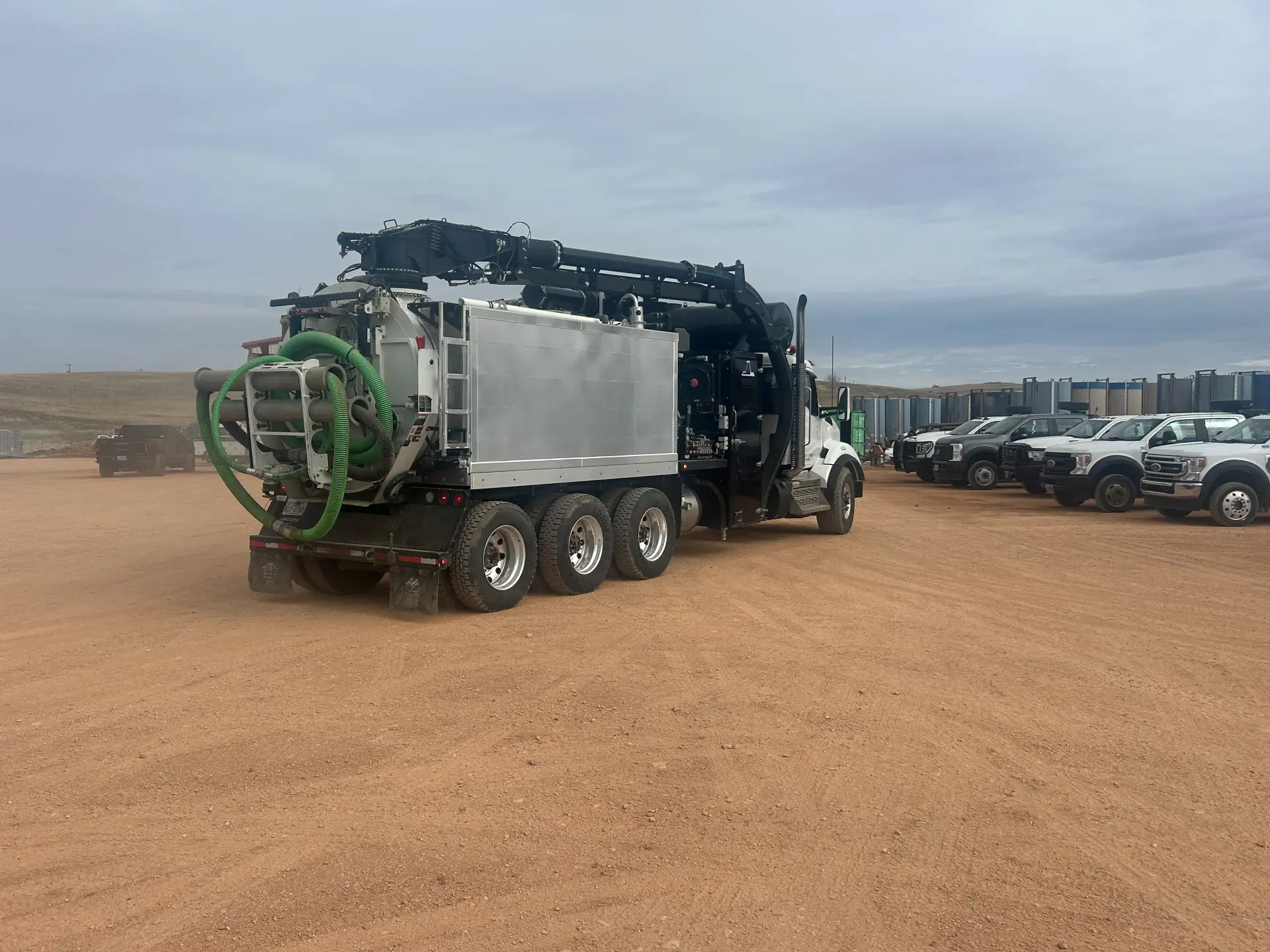 Rear view of a WOS hydrovac truck on a Bakken pad with WOS pickup fleet in the background