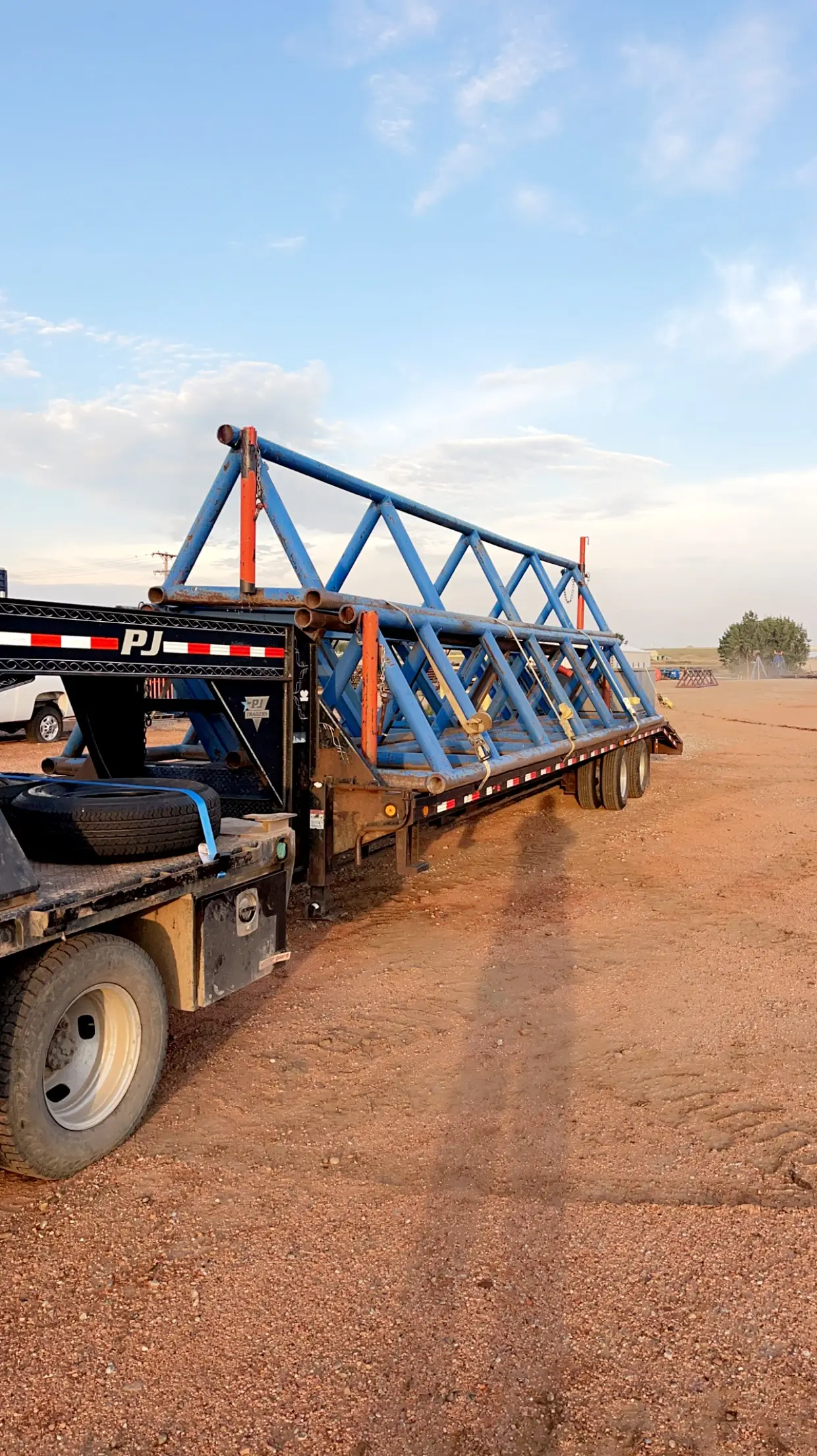 PJ gooseneck flatbed rental trailer hauling a folded blue catwalk at sunset