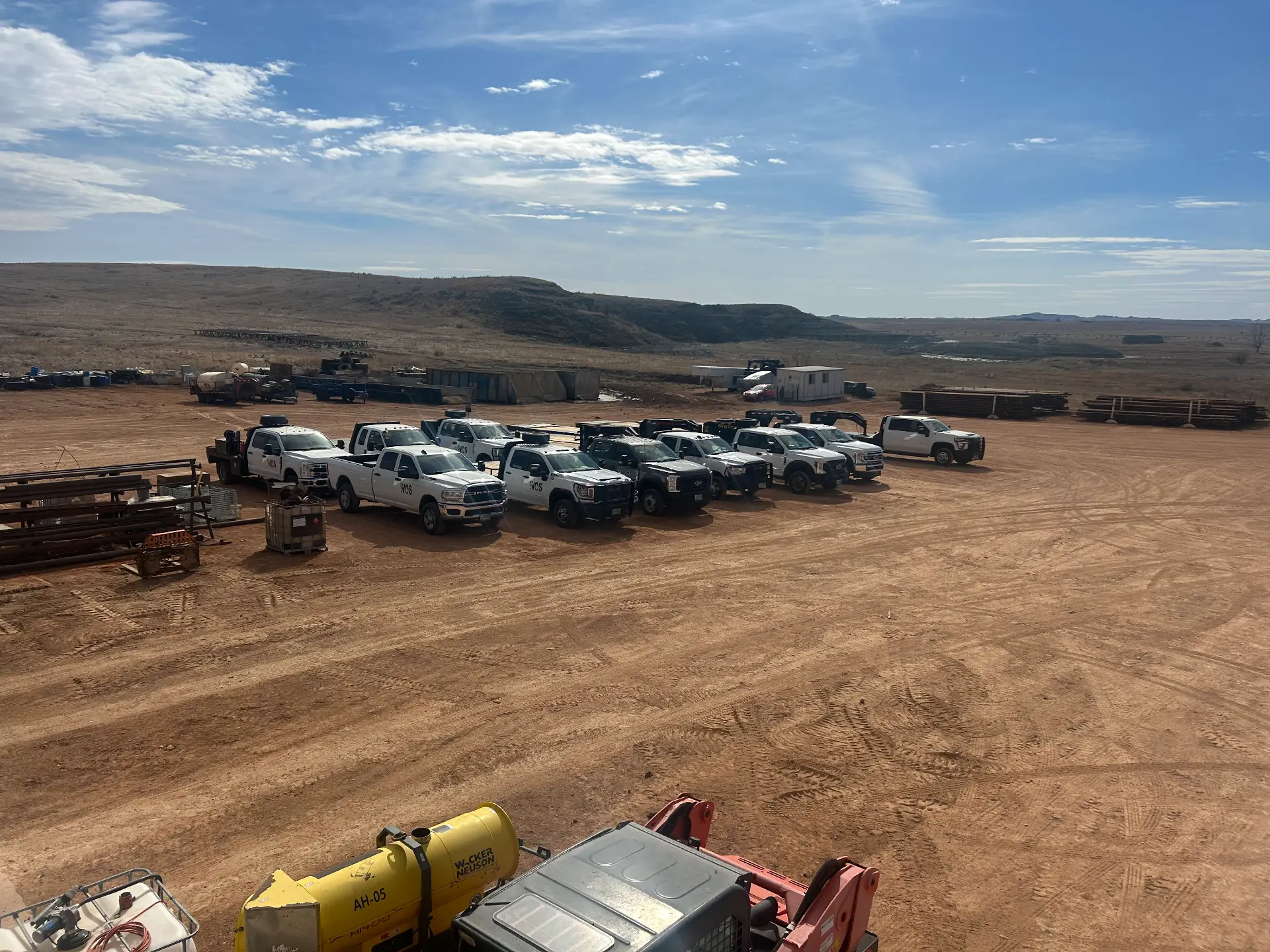 WOS service trucks and a Wacker Neuson light tower staged at a wide Bakken yard with pipe stacks